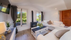 Un salon moderne avec un canapé blanc, une table basse, un téléviseur fixé au mur et une grande fenêtre avec des rideaux.