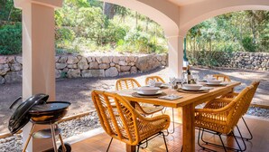 Une terrasse extérieure avec un mur en pierre, un barbecue, des chaises en osier et une table à manger pour quatre personnes.