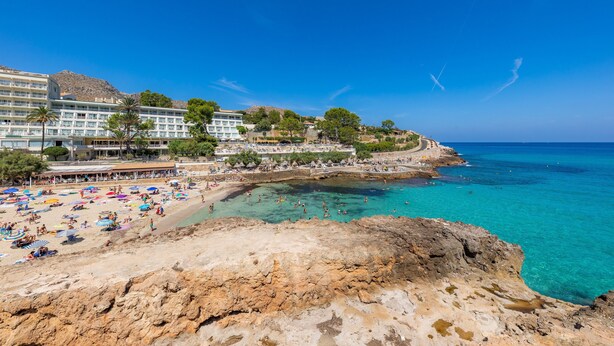 Un hôtel situé sur la côte, avec une plage, un rivage rocheux et une mer d’un bleu limpide.