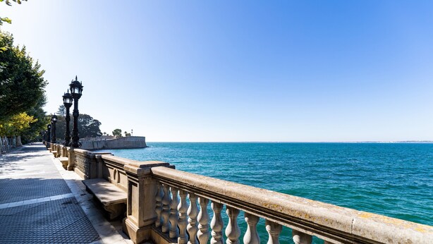 Una passeggiata lungomare con balaustra in pietra, percorso piastrellato e vista sul mare.