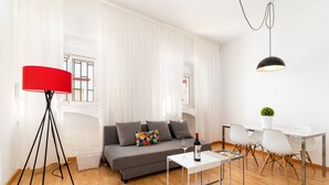 Un soggiorno moderno con un divano grigio, una lampada da terra rossa, un tavolino da caffè bianco e un'area pranzo con sedie bianche e un tavolo in vetro.
