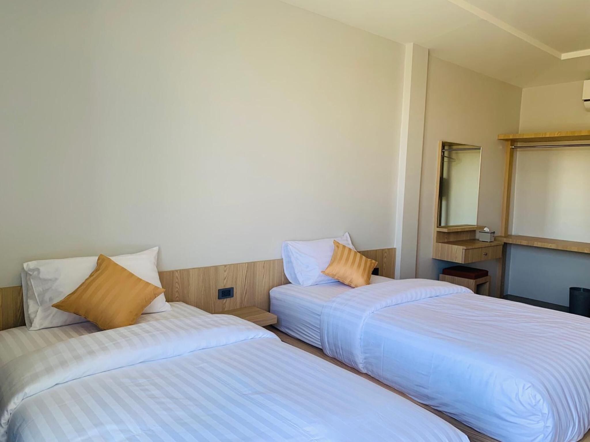 Een hotelkamer met twee bedden, elk voorzien van wit beddengoed en een houten hoofdeinde. Tussen de bedden staat een klein houten nachtkastje, en erboven hangt een spiegel.