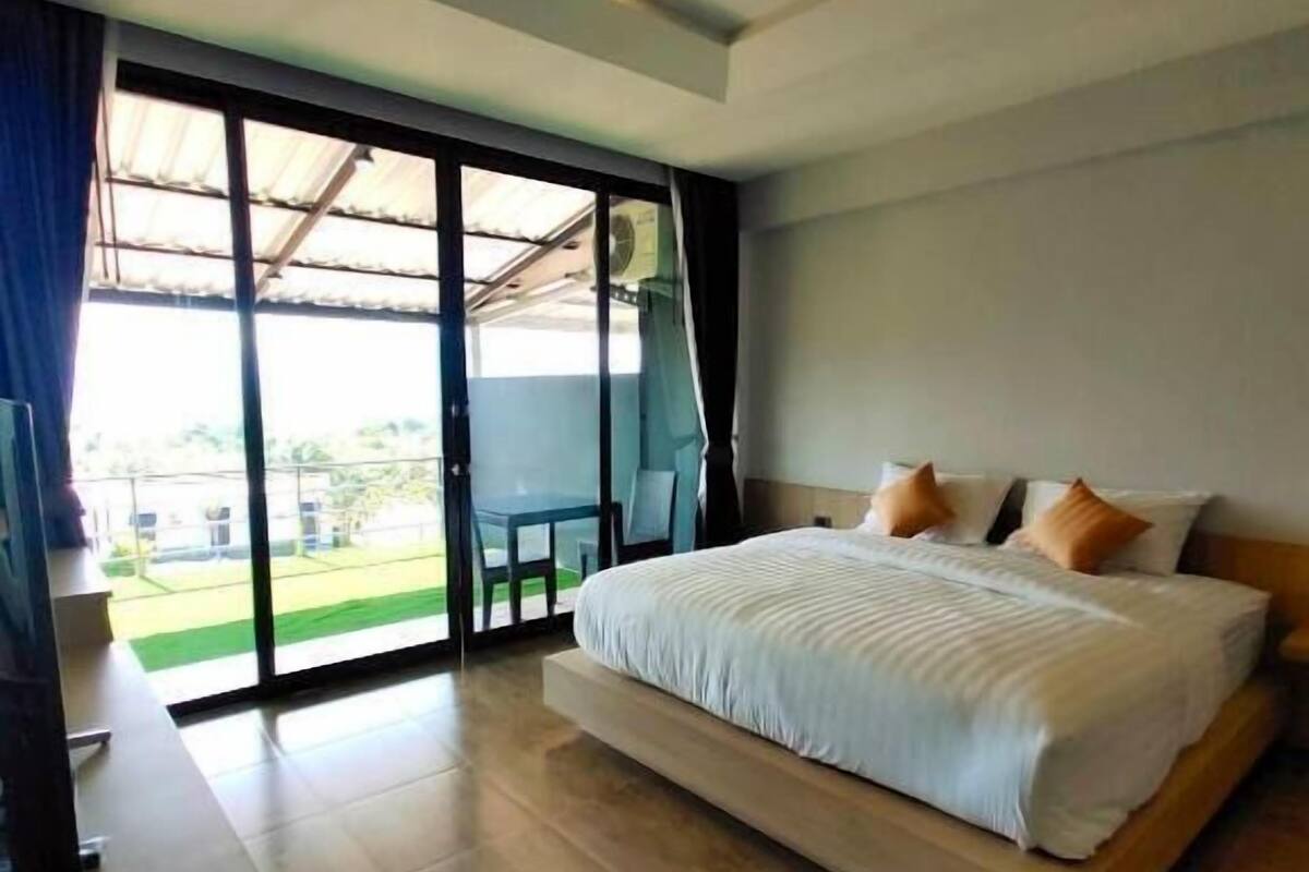 Une chambre moderne avec un grand lit, une télévision et une porte-fenêtre coulissante donnant sur un balcon.
