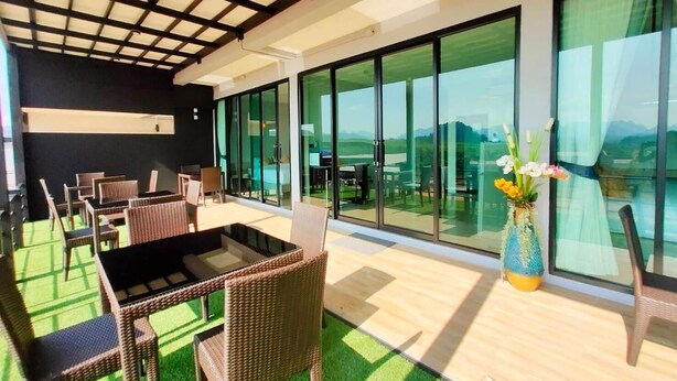 Een moderne buitenruimte met rieten meubels, een glazen eethoek en uitzicht op het landschap.