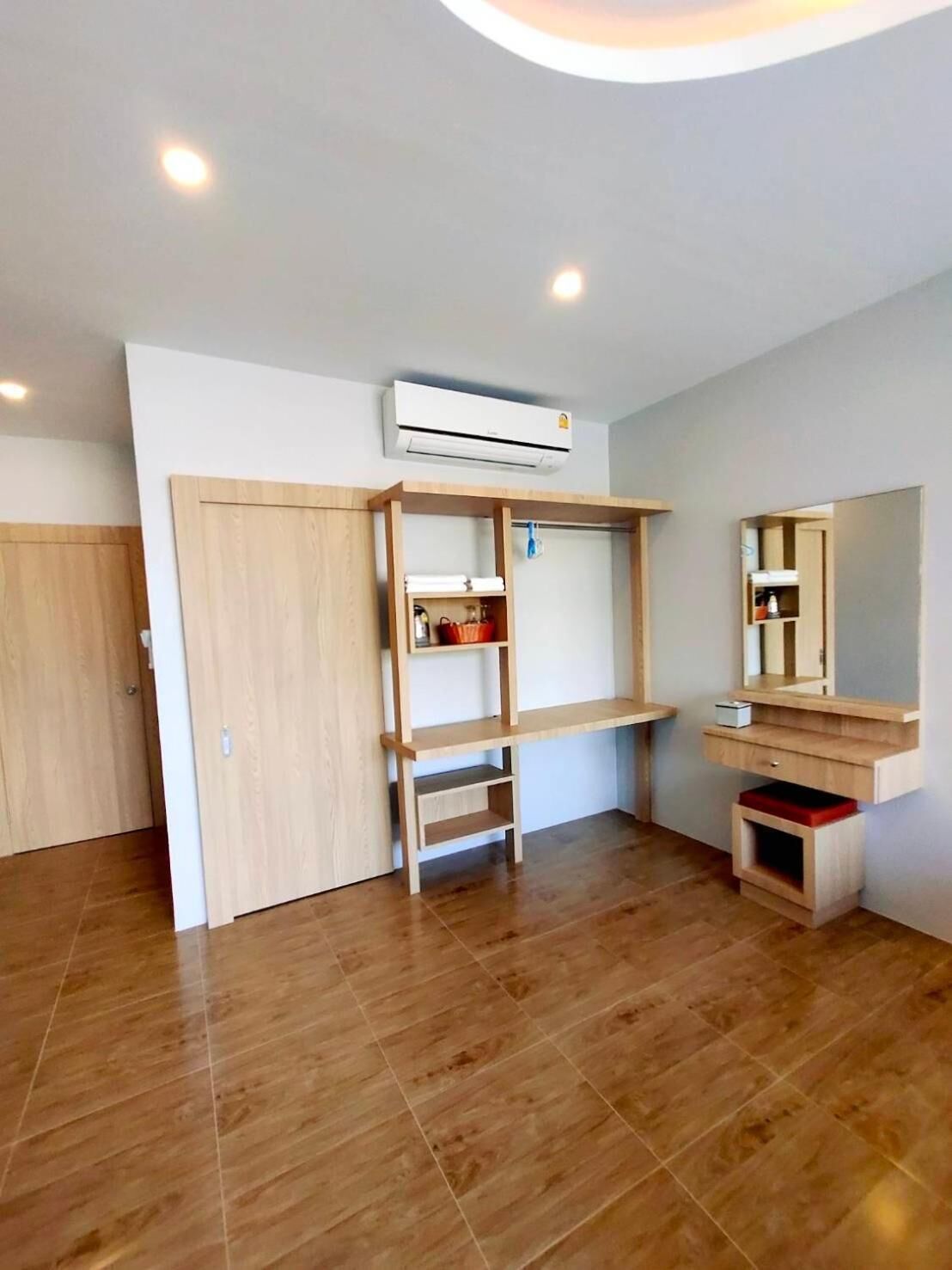 A room with a wooden wardrobe, a built-in shelf, a mirror, and an air conditioning unit.