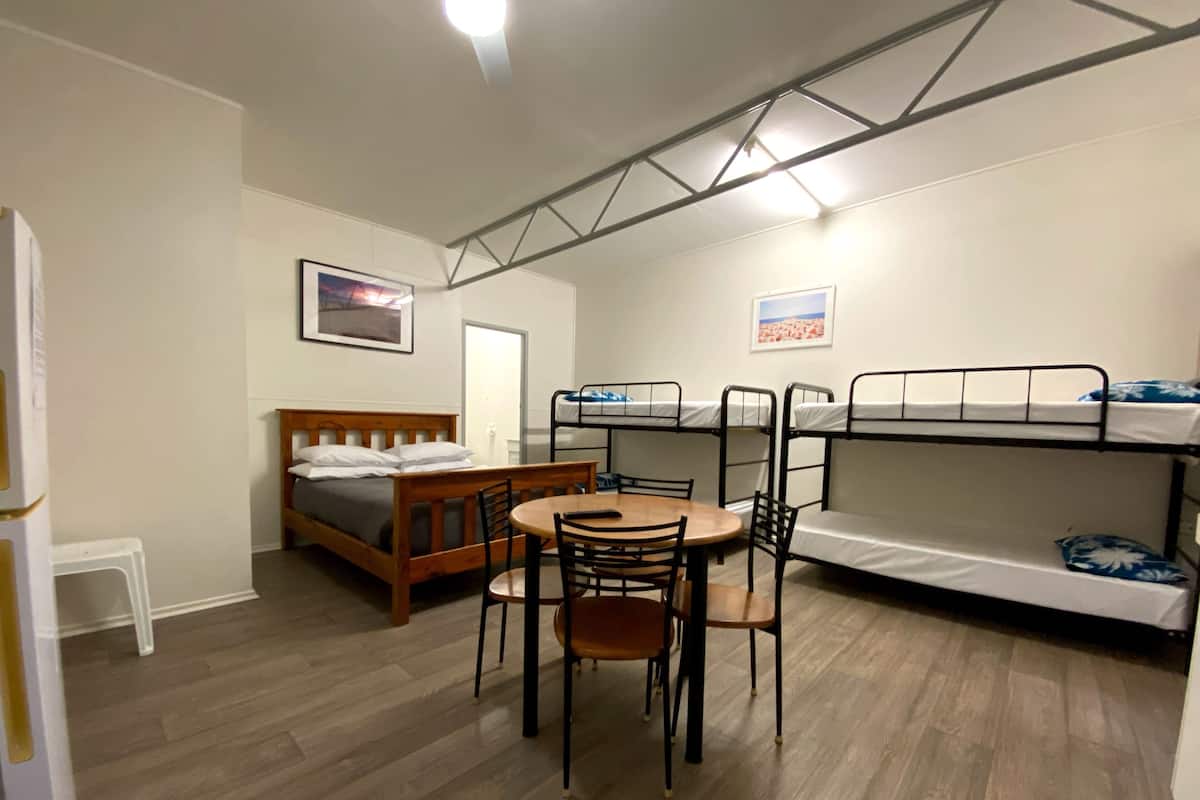 A compact room with a bed, bunk beds, a dining table with chairs, and a small white stool.