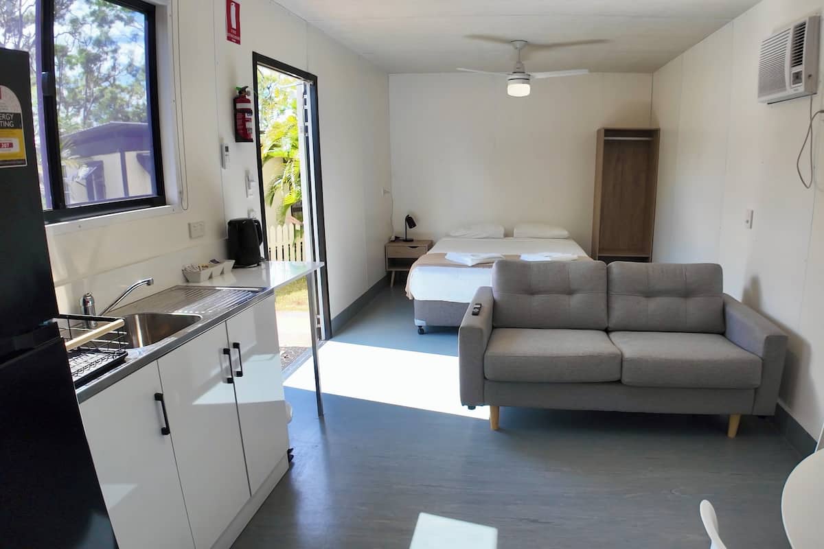 A compact hotel room with a kitchenette, a bed, a sofa, and a dining area.