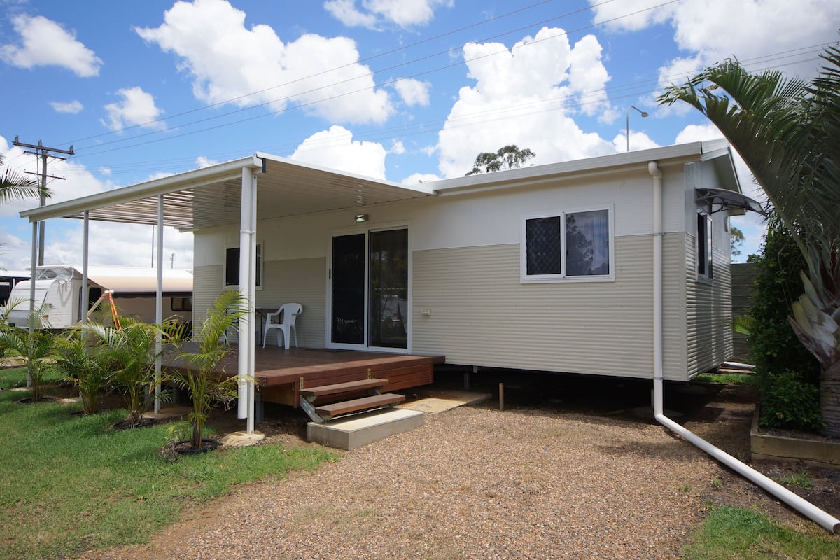 A single-story mobile home with a covered porch, a small front yard with gravel and plants, and a clear sky.