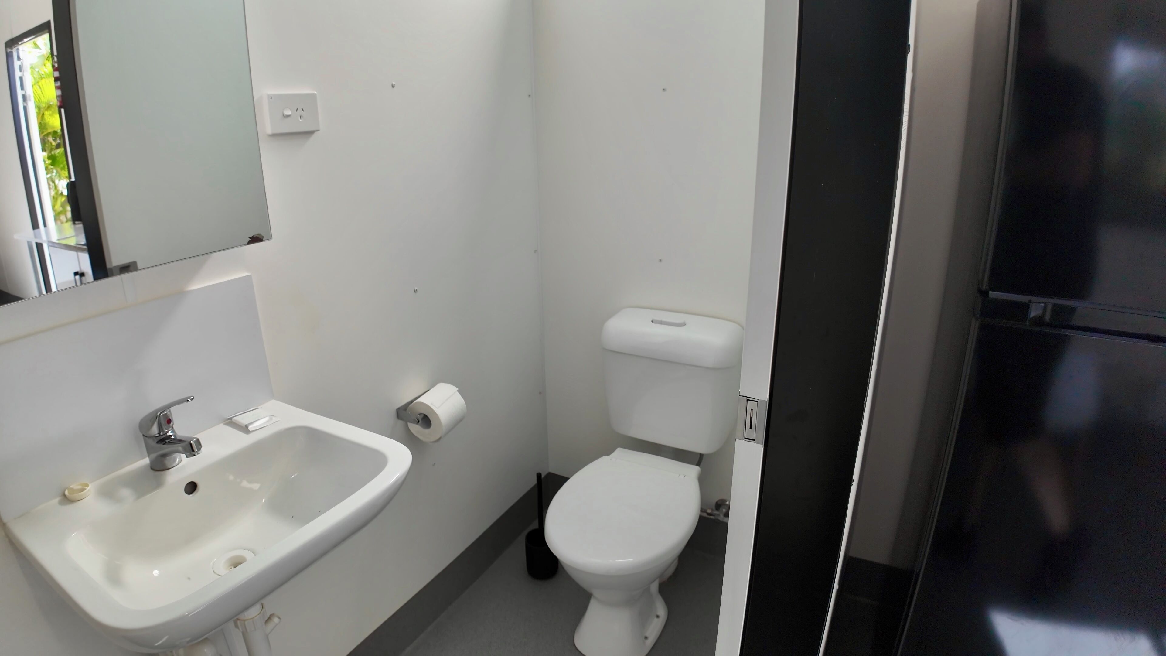 Et lille, rent badeværelse med hvid vask, toilet og et spejl.
