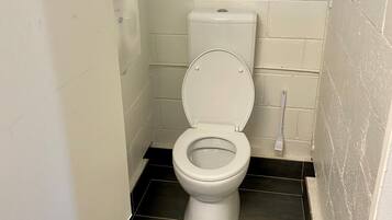 A small, white toilet in a tiled bathroom with a black floor.