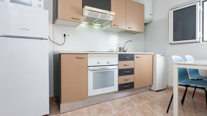 A compact kitchen with a refrigerator, oven, and microwave, wooden cabinets, and a window.