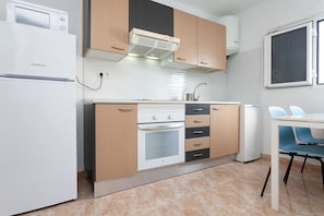 Une cuisine compacte équipée d’un réfrigérateur, d’un four et d’un four à micro-ondes, avec des meubles de rangement en bois et une fenêtre.