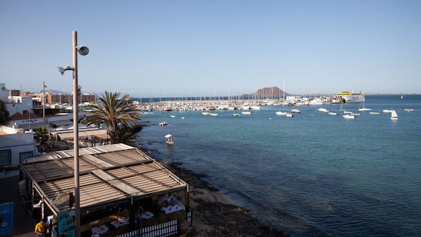 A coastal marina with boats, a clear sky, and a building with a flat roof.