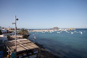 A coastal marina with boats, a clear sky, and a building with a flat roof.