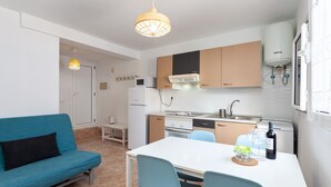A compact kitchen with a white refrigerator, stove, and sink, a dining table with chairs, and a blue sofa.