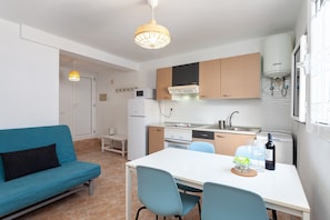 A compact kitchen with a white refrigerator, stove, and sink, a dining table with chairs, and a blue sofa.