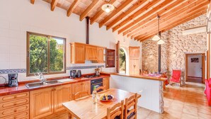 A kitchen with wooden cabinets, a central island, a dining area, and a stone wall. - Country House 'Sa Pova' with Mountain View, Wi-Fi and Air Conditioning (Alcúdia)