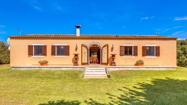 A two-story building with a tiled roof, a central entrance with a stone archway, and a small front garden. - Country House 'Sa Pova' with Mountain View, Wi-Fi and Air Conditioning (Alcúdia)