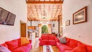A spacious living area with red sofas, a wooden ceiling, a TV, and a kitchen in the background. - Country House 'Sa Pova' with Mountain View, Wi-Fi and Air Conditioning (Alcúdia)