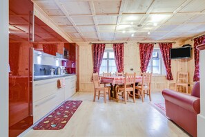 A compact kitchen with modern appliances, a dining area with wooden chairs, and a red sofa.