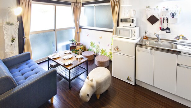 A compact kitchen with a microwave, sink, and various utensils. There's a sofa and a dining table with a decorative animal figure. - Espoir Omorimachi (Tokyo)