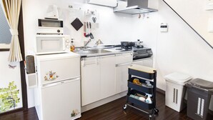 A compact kitchen with a microwave, stove, sink, and a small refrigerator. There is a cart with cleaning supplies and two trash bins. - Espoir Omorimachi (Tokyo)