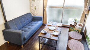 A living room with a blue sofa, a wooden coffee table, and a small round table with a book and a plant. - Espoir Omorimachi (Tokyo)
