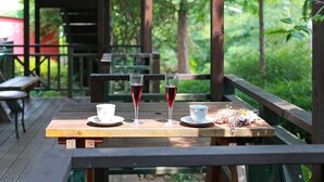 A wooden deck with a table set for two, featuring two glasses of red wine, a white cup, and a saucer. - Gyeongju Europe Village Pension (Gyeongju)