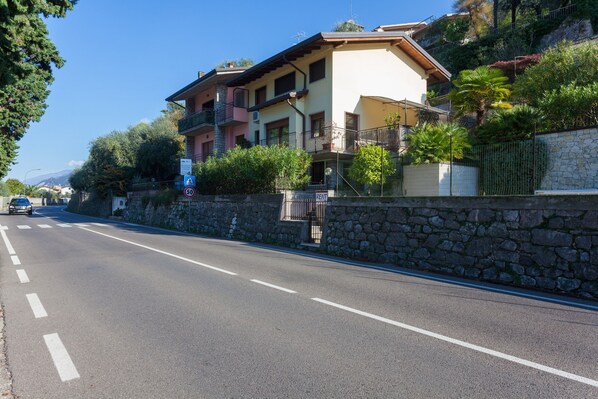 A multi-story building with balconies, a stone wall, and a clear road. - Holiday Apartment "Randa" On Lakeside with Balcony, Terrace and Stunning View (Malcesine)