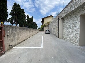 Uma área de estacionamento com um carro, um muro de pedra e um edifício ao fundo.