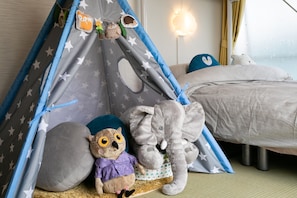 A child's play tent with star patterns, a plush elephant, and a stuffed owl in a hotel room.