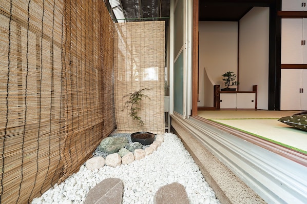 A traditional Japanese room with tatami flooring, a shoji screen, a bonsai tree, and a small table with a plant.