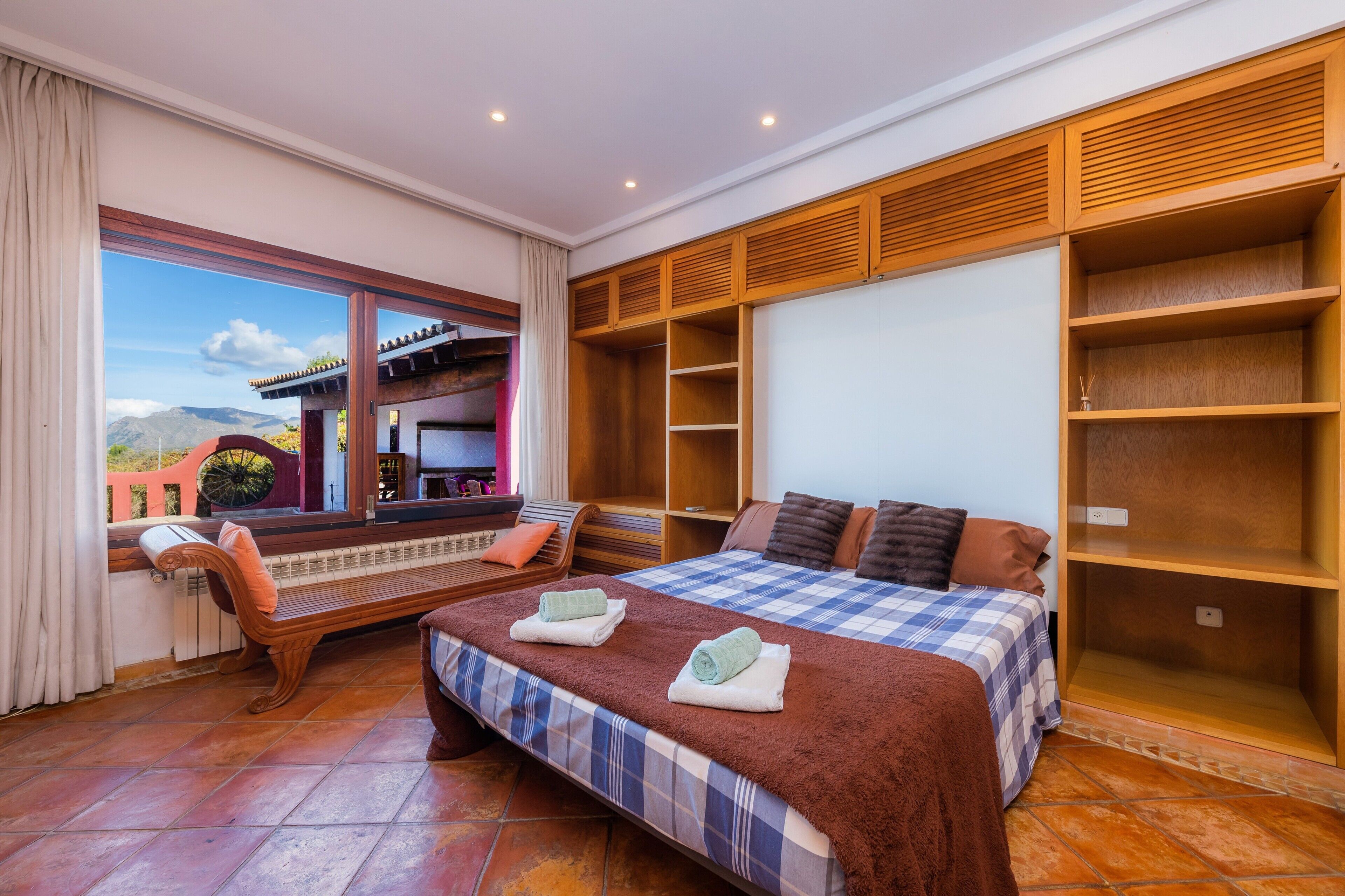 Un dormitorio con una cama grande, un armario de madera, un banco junto a la ventana y vistas a las montañas.