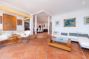 Un espacio habitable amplio con un sofá blanco, sillas modernas, una mesa de centro de vidrio y piso de baldosas.