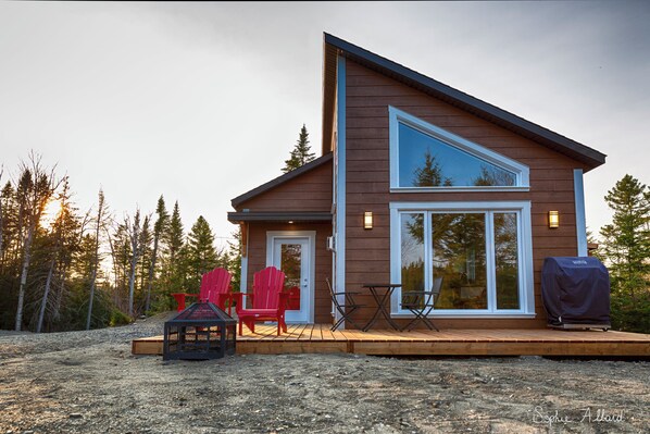 A modern house with a deck, red chairs, and a grill.