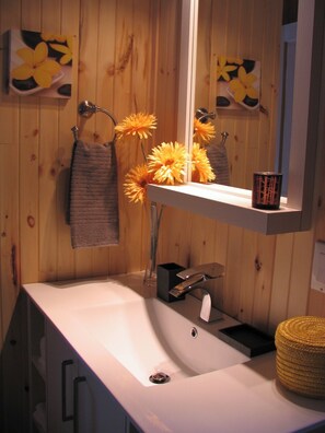 A bathroom with wooden paneling, a white sink, a mirror, a towel rack, and a vase with yellow flowers.