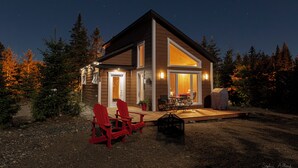 Ein modernes Haus mit einer Terrasse, zwei roten Adirondack-Stühlen und einem überdachten Grillbereich.