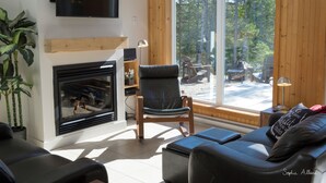 A modern living room with a fireplace, a sofa, a chair, and a large window offering a view of the outdoors.
