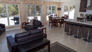 A modern living room with a leather sofa, a dining area with wooden chairs, and a kitchen with a bar counter.