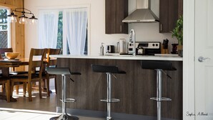 A modern kitchen with dark wood cabinets, a stainless steel range hood, and a bar area with stools.