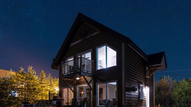 A two-story wooden house with a balcony, large windows, and a deck area.