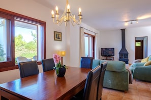 Un comedor con una mesa de madera, sillas, una araña, un televisor y una chimenea.