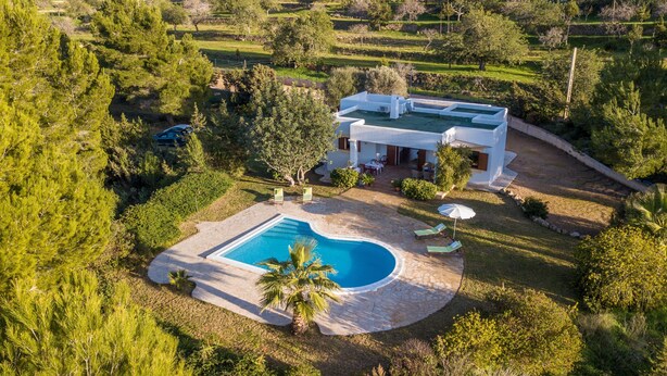 Une maison moderne dotée d’une piscine, entourée d’une végétation luxuriante et accessible par un chemin de pierre.