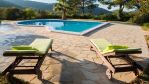 Une piscine bordée de deux chaises longues, entourée de carreaux de pierre et de verdure.
