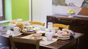 A dining table with various breakfast items, including bowls, mugs, and a fruit bowl.