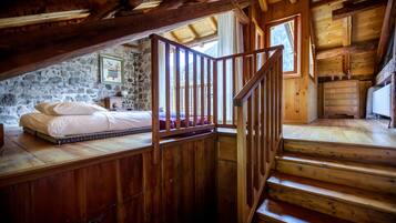 A wooden interior with a loft bedroom, stone wall, wooden staircase, and a dresser.