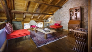 A rustic room with a wooden ceiling, a red sofa, a wooden cabinet, and a patterned rug.