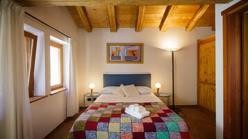 A bedroom with a wooden ceiling, a bed with a colorful quilt, two bedside lamps, and a painting on the wall.