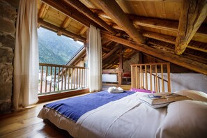 A bedroom with a wooden ceiling, a bed with white and blue bedding, a window with curtains, and a view of mountains. - Cosy Holiday Home "La Pita" with Mountain View, Balcony, Fireplace and Wi-Fi (La Valle Agordina)