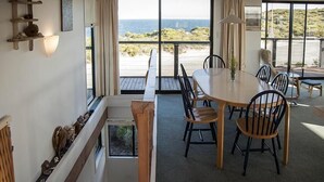A dining area with a large table and chairs, a staircase, and a view of the sea.